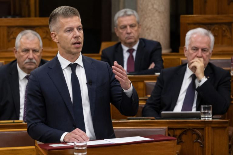 Magyar Péter beszédet mond az Országgyűlésben, miközben több politikus feszült arccal figyeli.